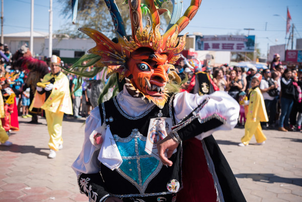 Foto de uma pessoa, em primeiro plano, vestida tipicamente na Festa de La Tirana, no Chile; ao fundo, uma multidão.